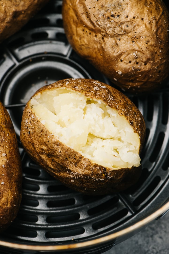 A baked potato sliced open in the basket of an air fryer.