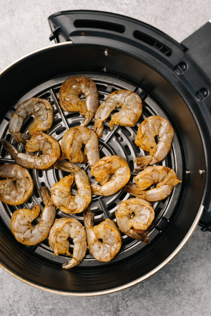 Marinated shrimp in the basket of an air fryer in an even layer.