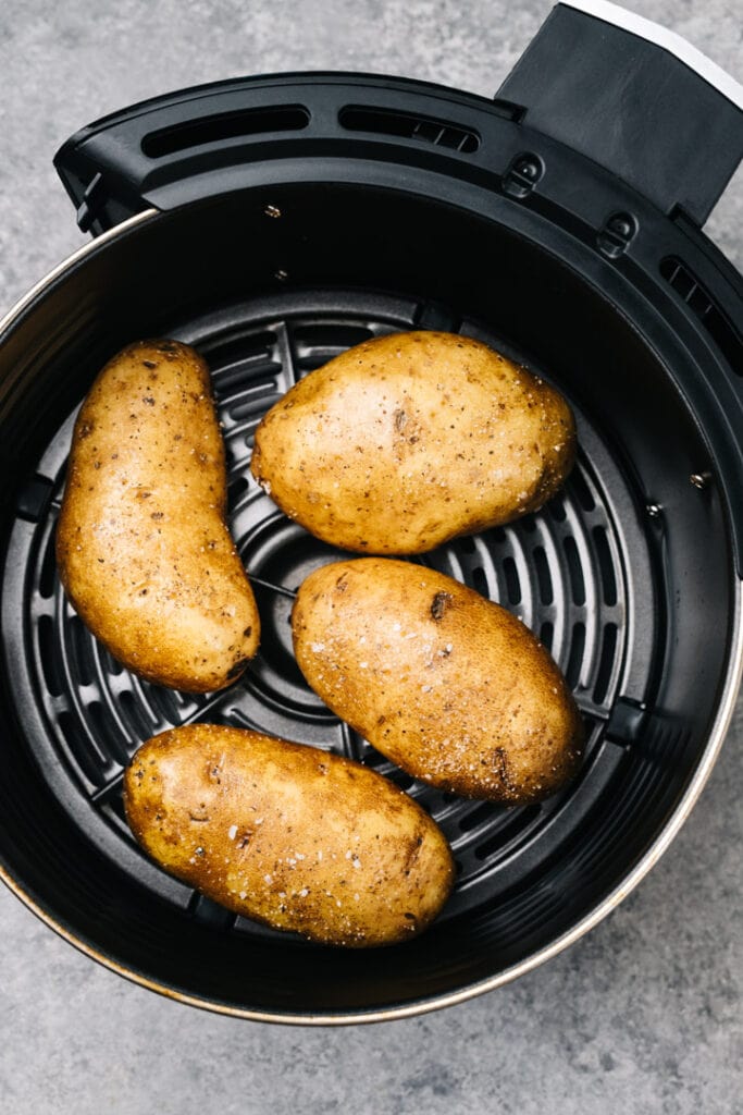 Four potatoes rubbed with olive oil and sprinkled with salt arranged in an air fryer basket.