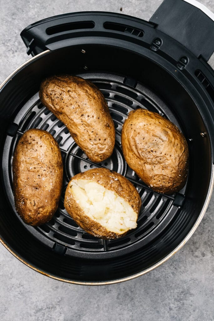 Four baked potatoes in the basket of an air fryer.