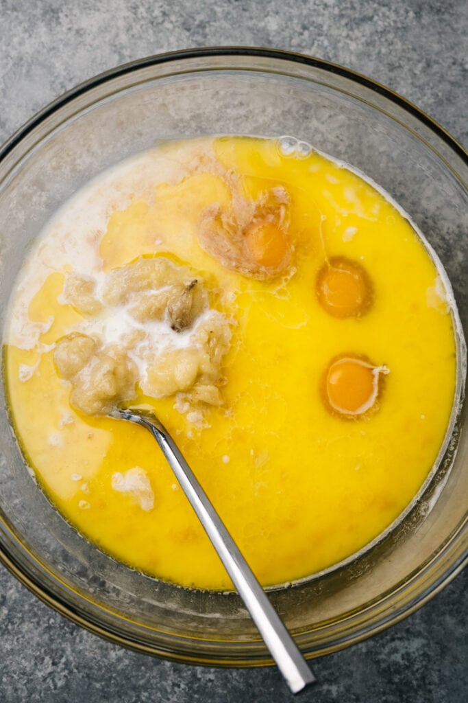 Mashed bananas, eggs, butter, and milk in a large mixing bowl with a fork.