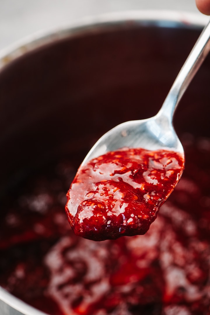 Berry compote on a silver spoon hovering over a pot.