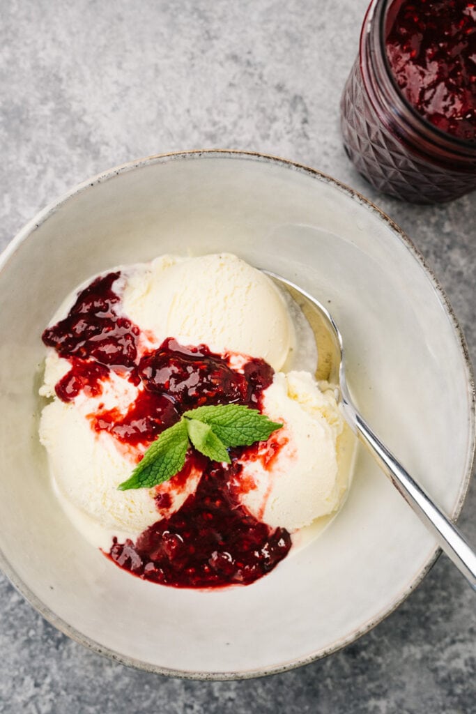 Vanilla ice cream drizzled with berry compote on a concrete background with a jar of berry compote to the side.