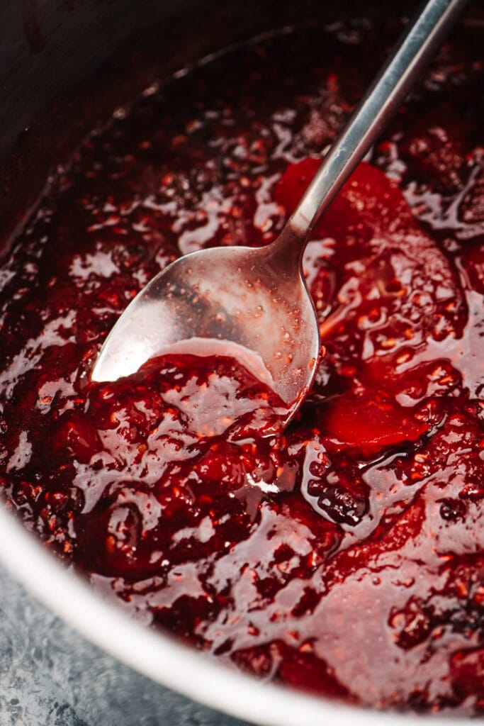 A silver spoon dipping into a pot of berry compote.