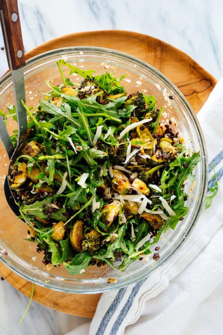 A vegetarian dinner salad with broccoli, arugula and lentils in a large glass serving bowl on a marble table. 