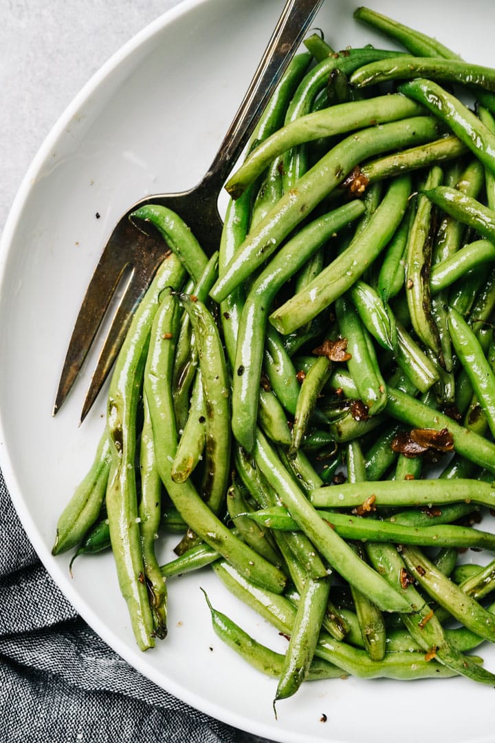 Sautéed green beans with garlic in a white serving bowl with a silver serving fork.