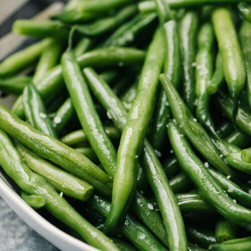 Side view, steamed green beans with butter, salt and pepper in a tan serving bowl.