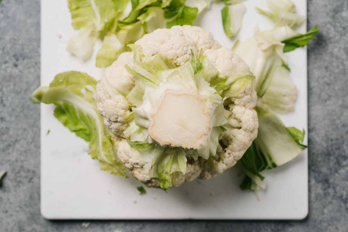 A head of cauliflower on a white cutting board with the leaves and stems removed.