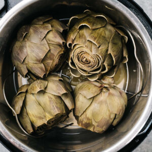 Four whole steamed artichokes in an instant pot.