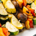 Side view, a stack of grilled vegetable kabobs on a white platter.