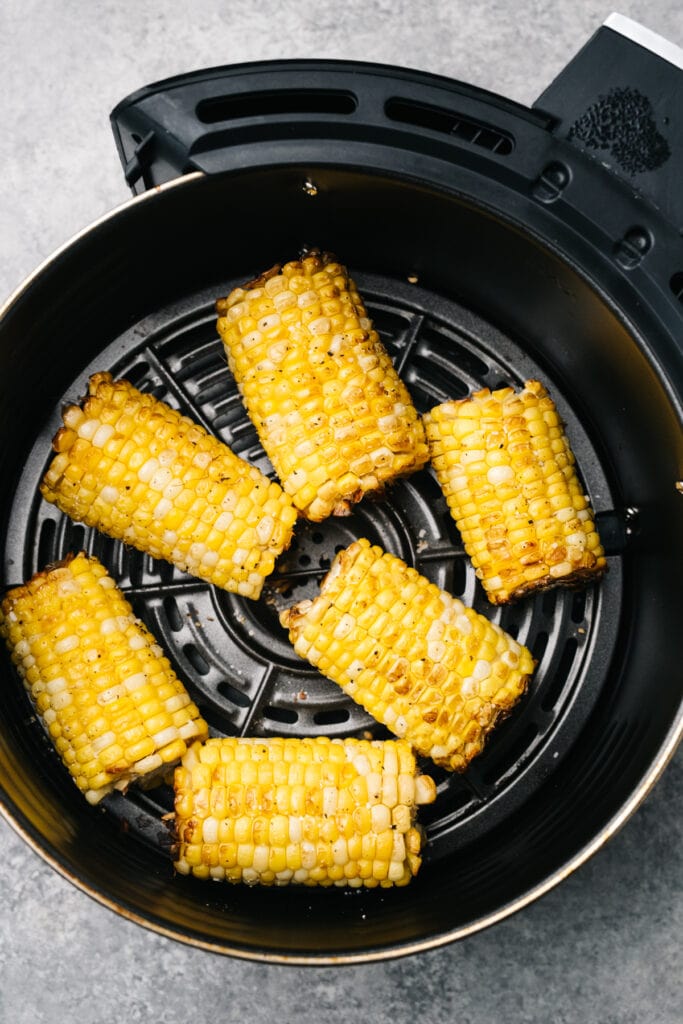 Cooked corn on the cob in a single layer in an air fryer basket.