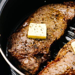 Side view, a cooked steak in an air fryer basket topped with a small pat of butter.