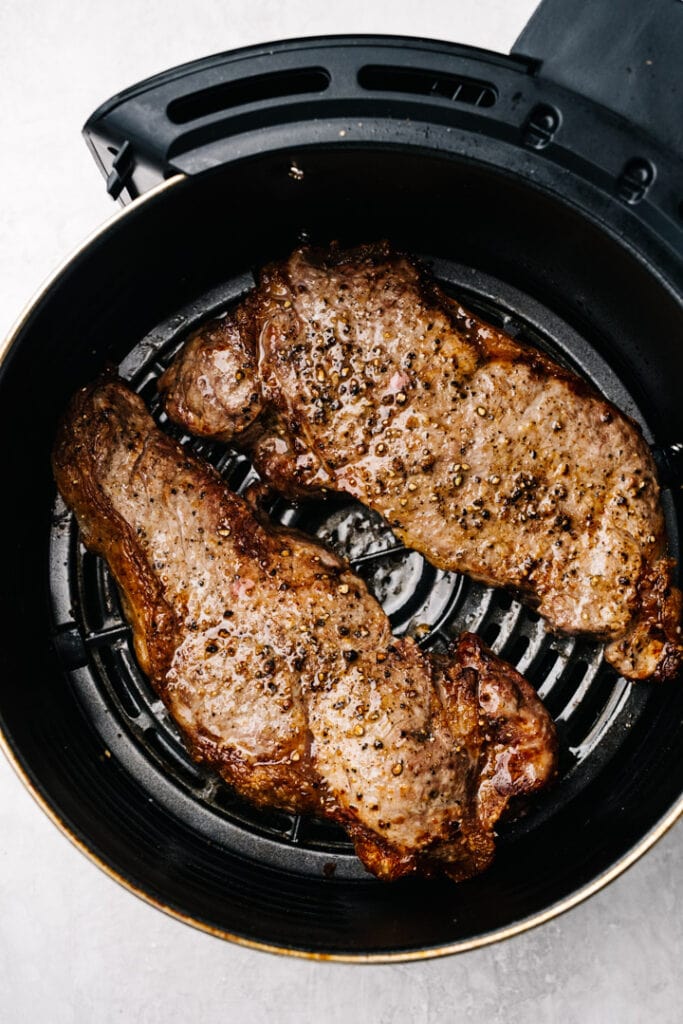 Two cooked ribeye steaks in the basket of an air fryer.