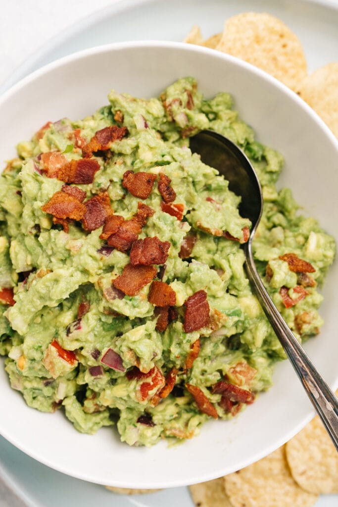 Bacon guacamole in a small white bowl surrounded by tortilla chips.