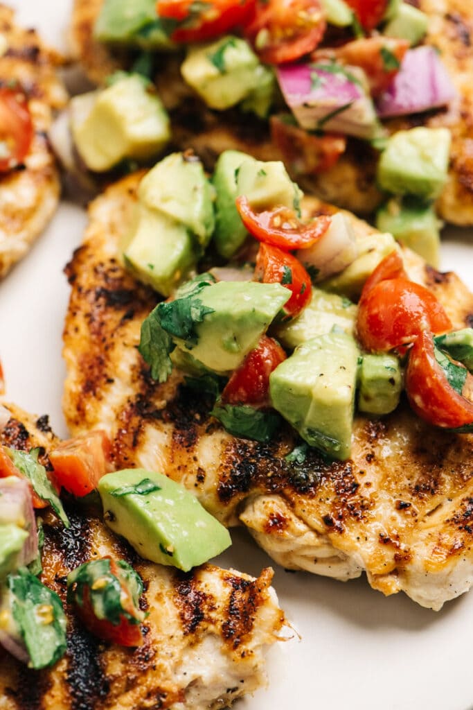 Side view, grilled chicken breasts topped with avocado tomato salsa.