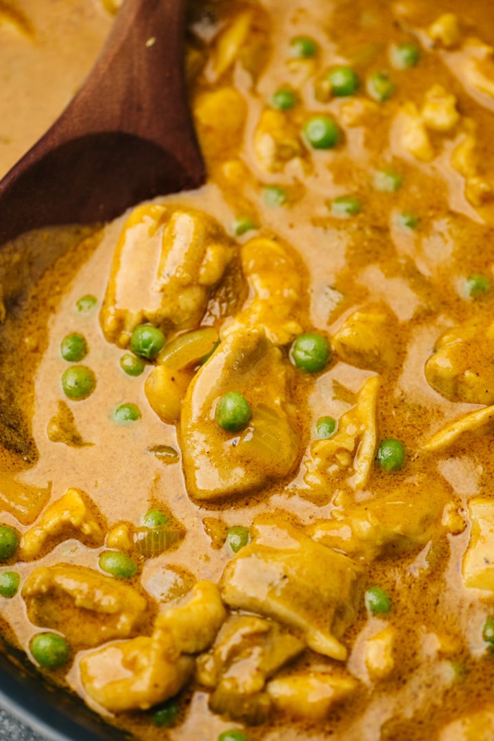 Side view, coconut curry chicken in a skillet with peas.