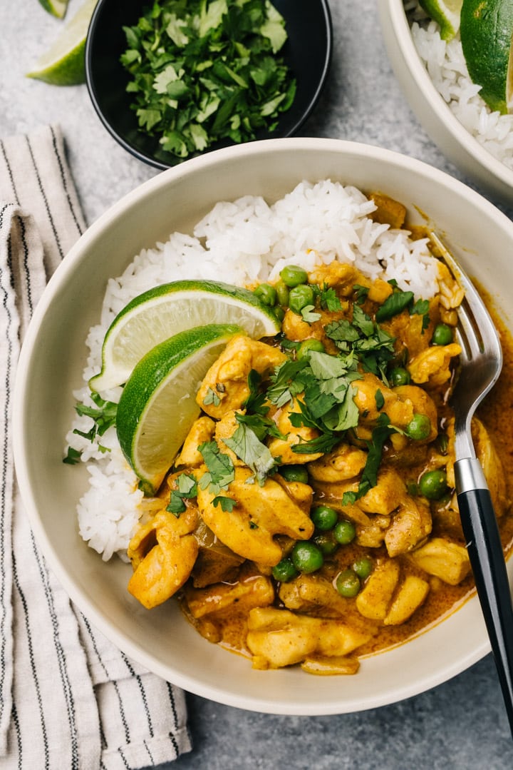 A bowl of coconut chicken curry served over rice with a lime wedges and fresh cilantro.