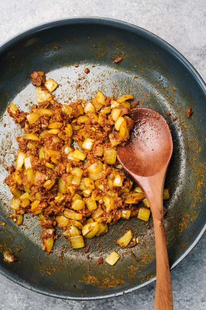 Onion, garlic, and ginger sautéed with tomato paste and curry spices in a skillet with a wood spoon.