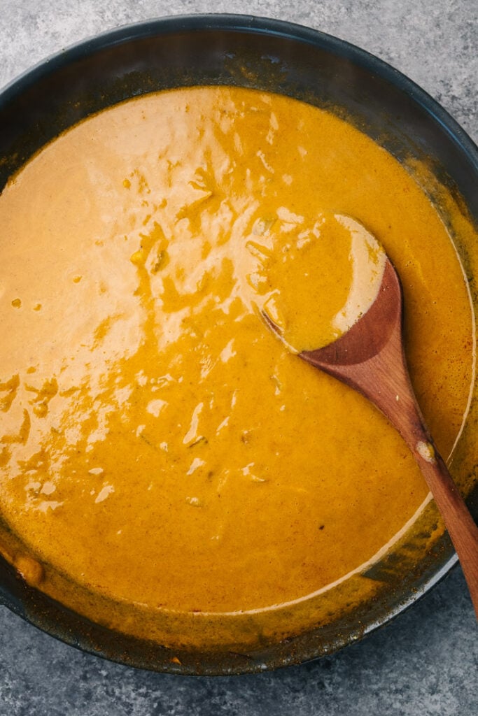 Coconut curry sauce in a skillet with a wood spoon.