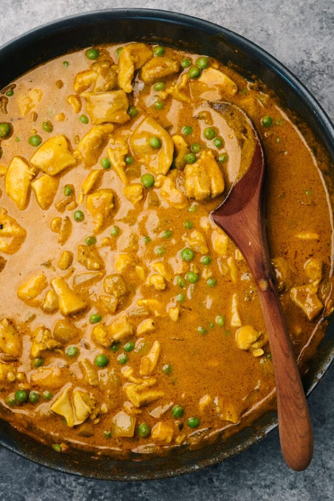 Coconut curry chicken in a skillet with peas.