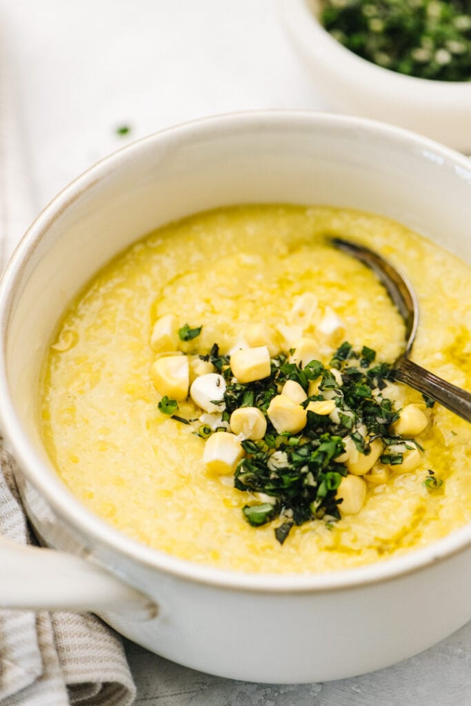 Side view, a bowl of summer corn soup garnished with herb gremolata.