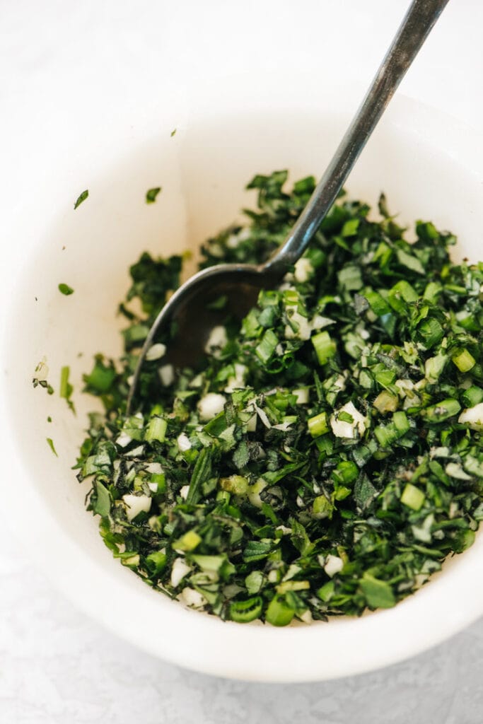 Fresh herb gremolata in a small marble bowl with a silver spoon.