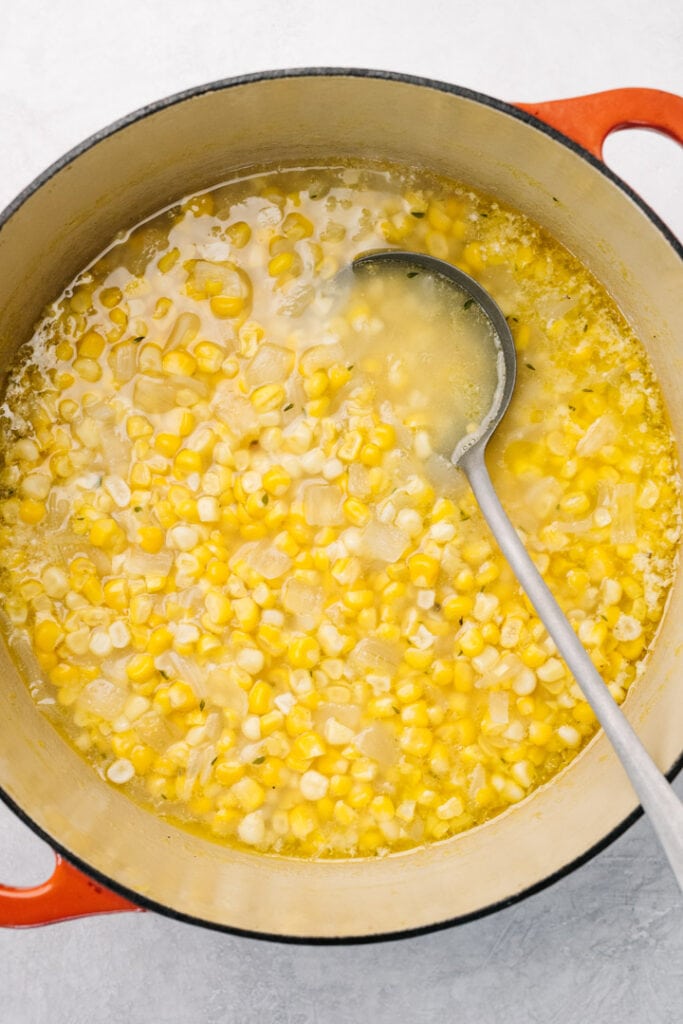 Fresh corn soup in a red dutch oven with a ladle, before being pureed.