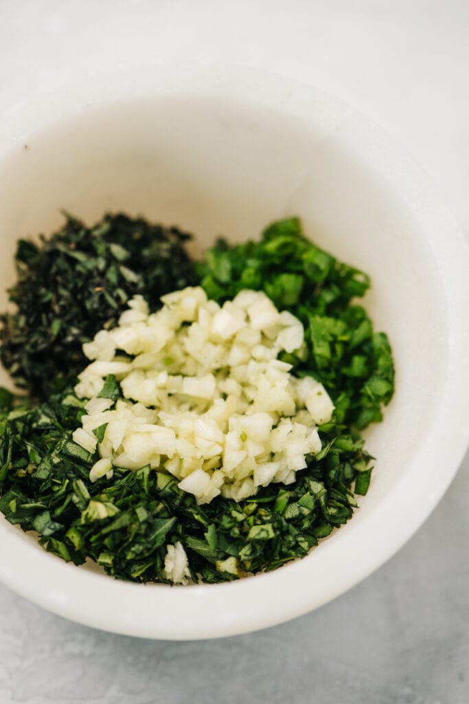 Fresh herbs and garlic in a small marble bowl before being mixed to make gremolata.