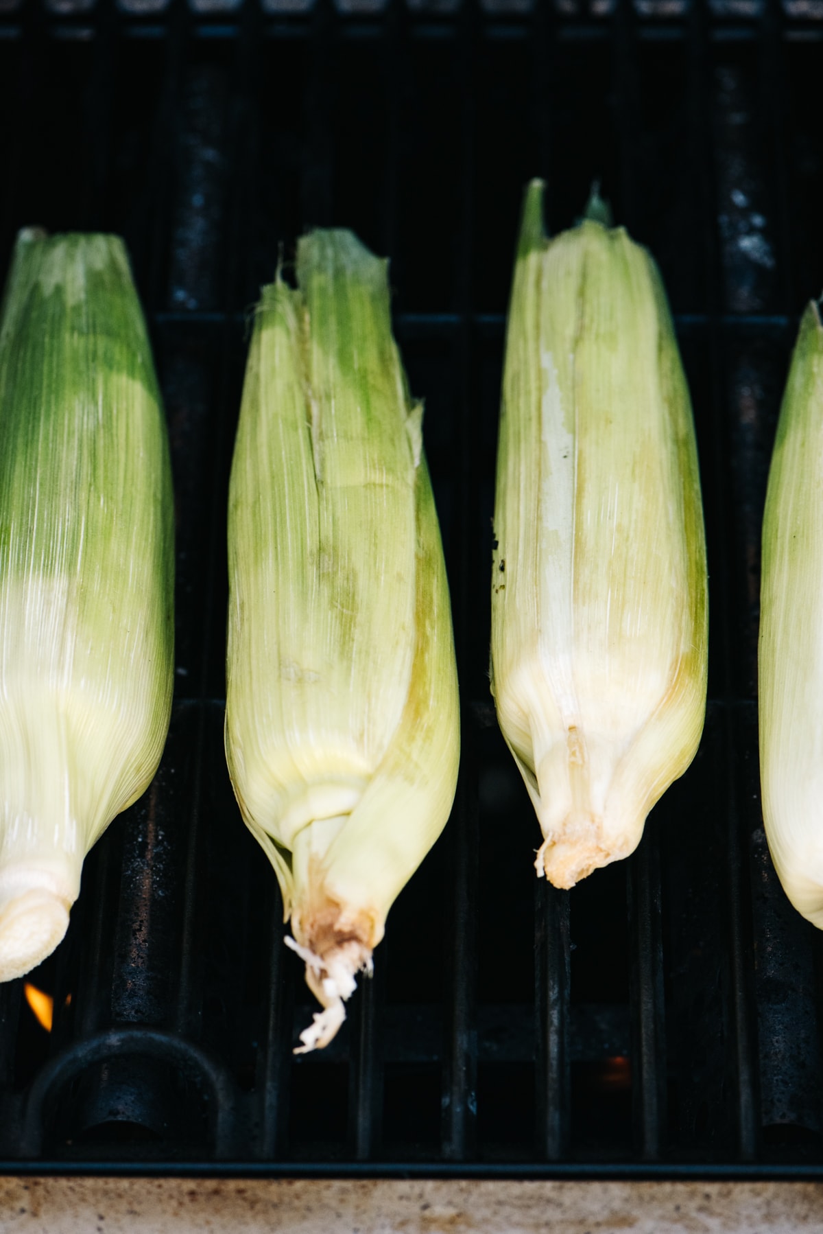 Four ears of corn in husks on a grill.