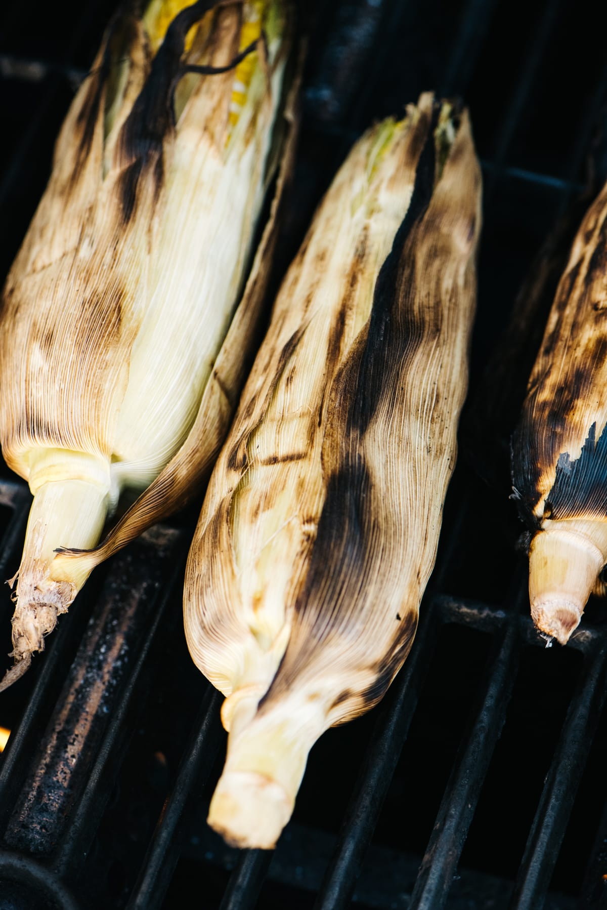 Four ears of corn on a gas grill, showing the husks very charred.
