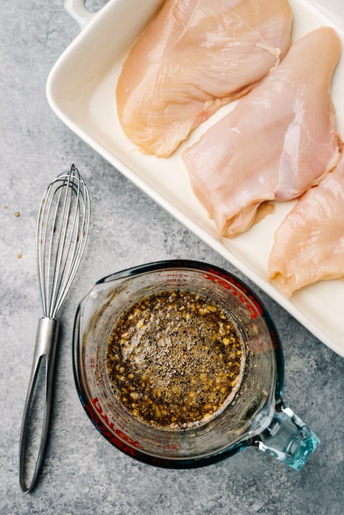 Healthy teriyaki sauce in a glass measuring cup next to chicken breasts in a casserole dish.