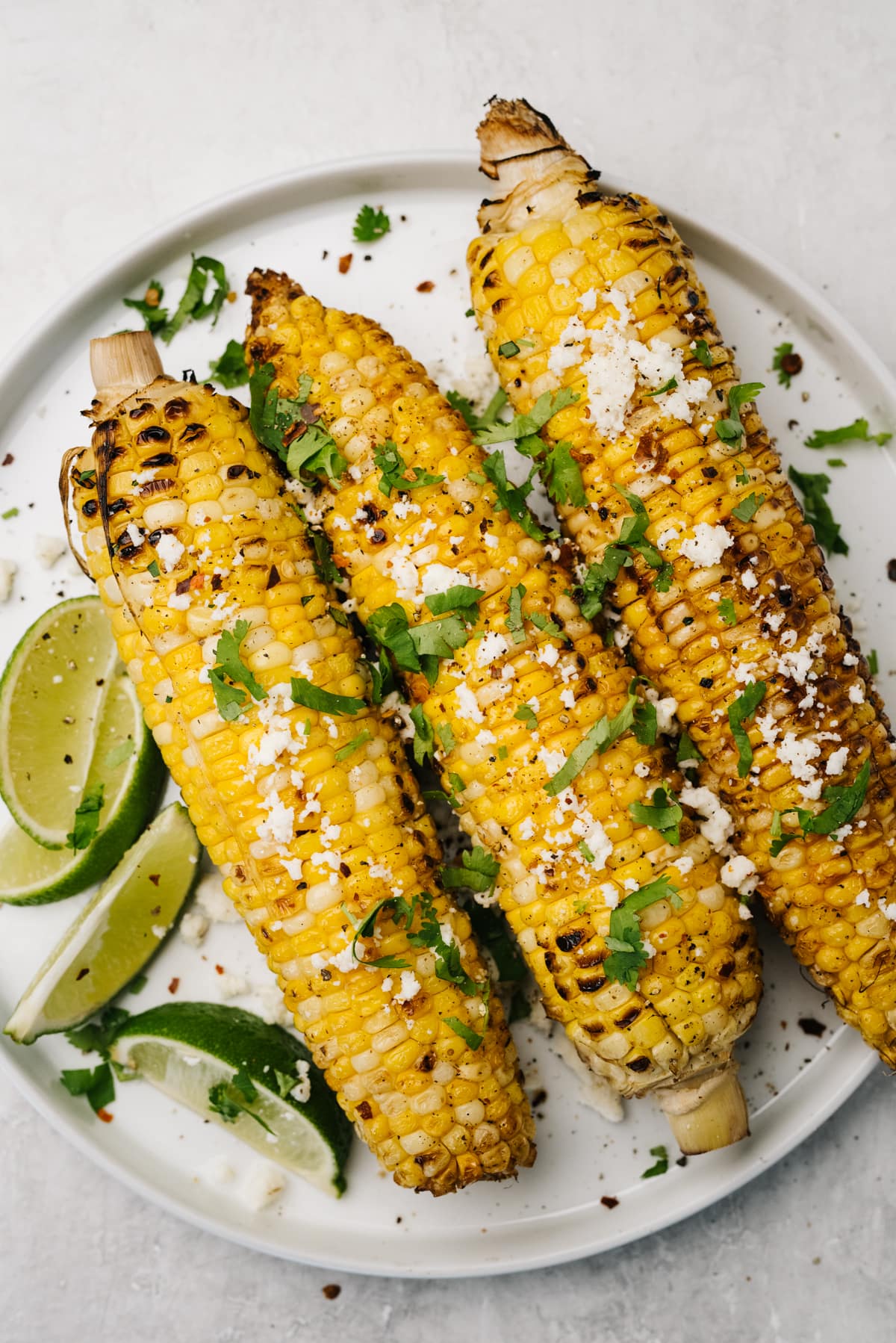 Three ears of grilled corn on the cob topped with lime juice, cilantro, and queso fresco cheese.