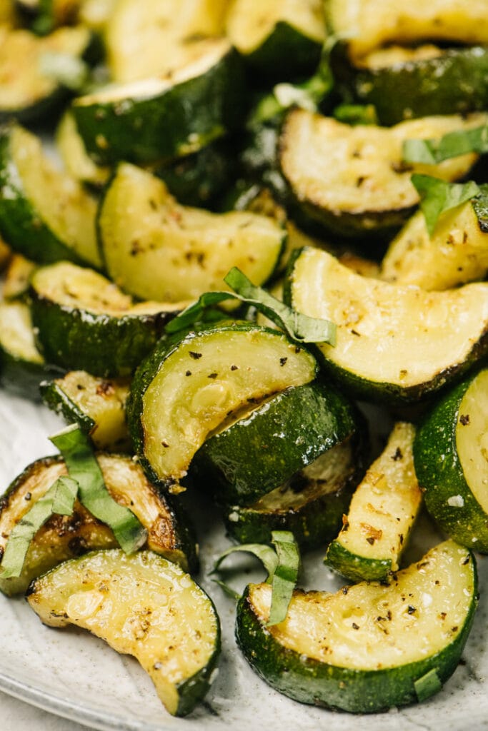 Air fryer zucchini on a white plate, garnished with fresh basil.