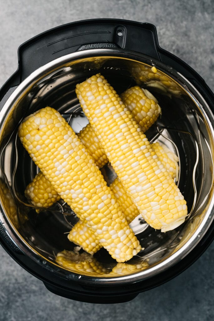 Four ears of corn with husks and silks removed layered in an instant pot.