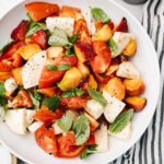 Diced peaches, diced tomatoes, fresh mozzarella, and basil tossed in a white serving bowl with a grey and white striped napkin.