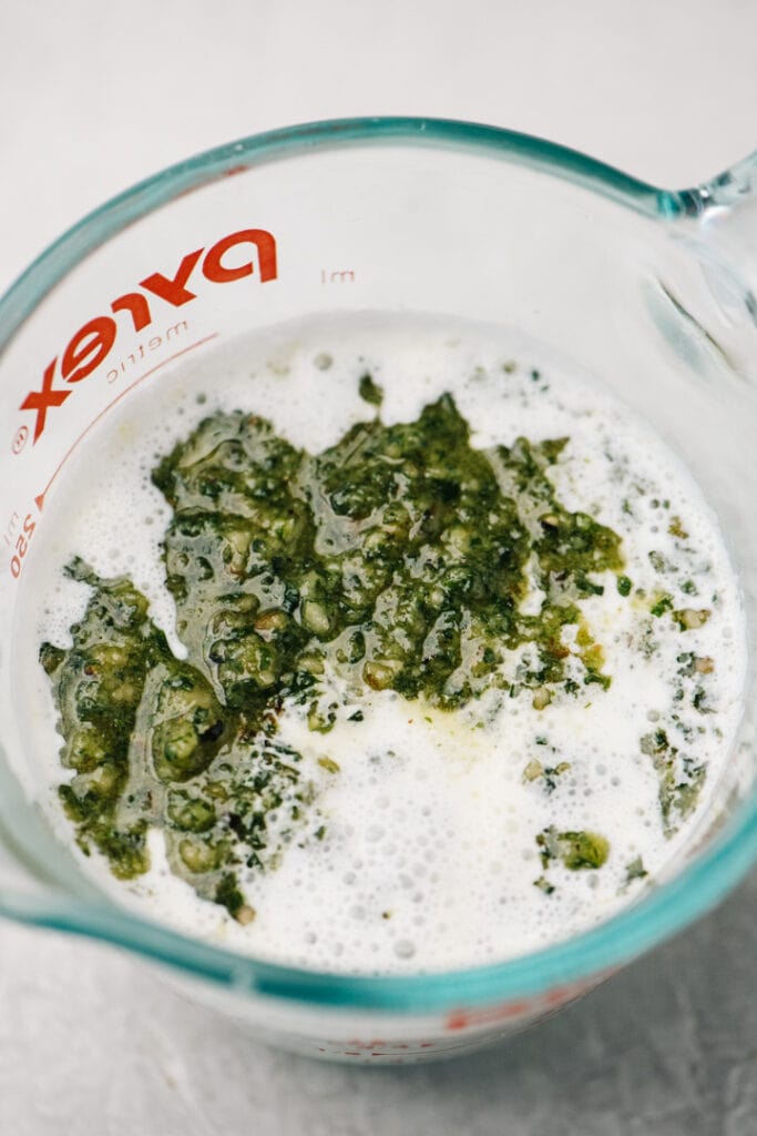Pesto sauce and heavy cream in a 1-cup measuring cup.