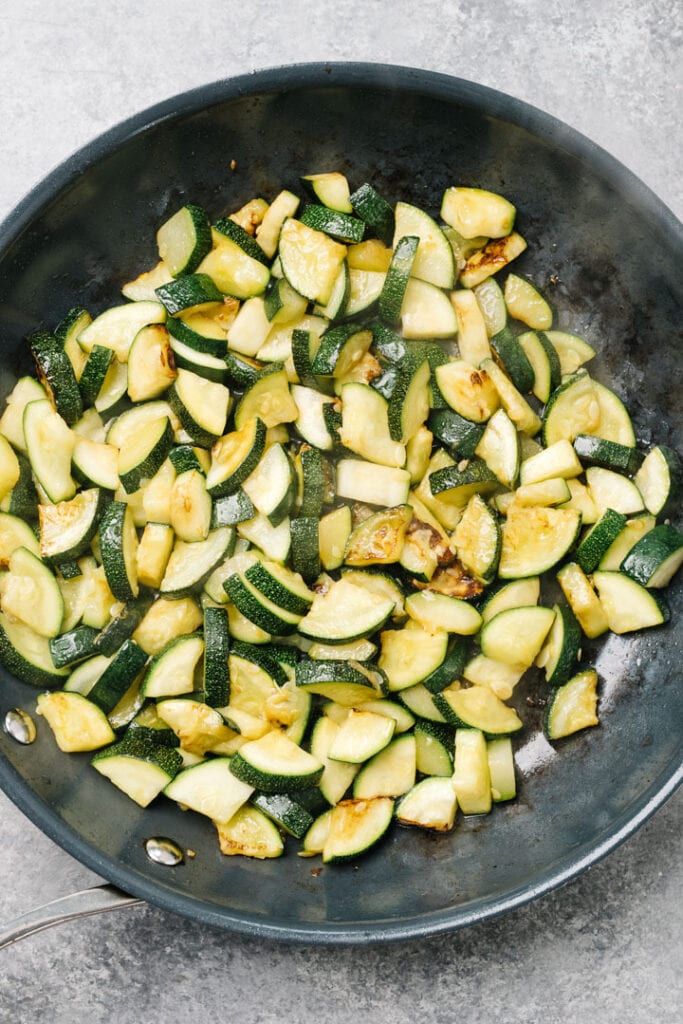 Chopped zucchini tossed with olive oil in a skillet.