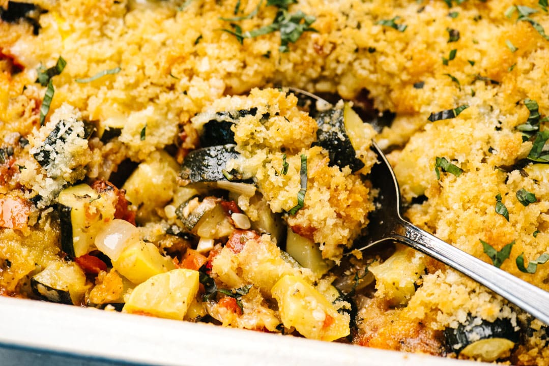 Side view, a silver serving spoon tucked into a zucchini casserole.