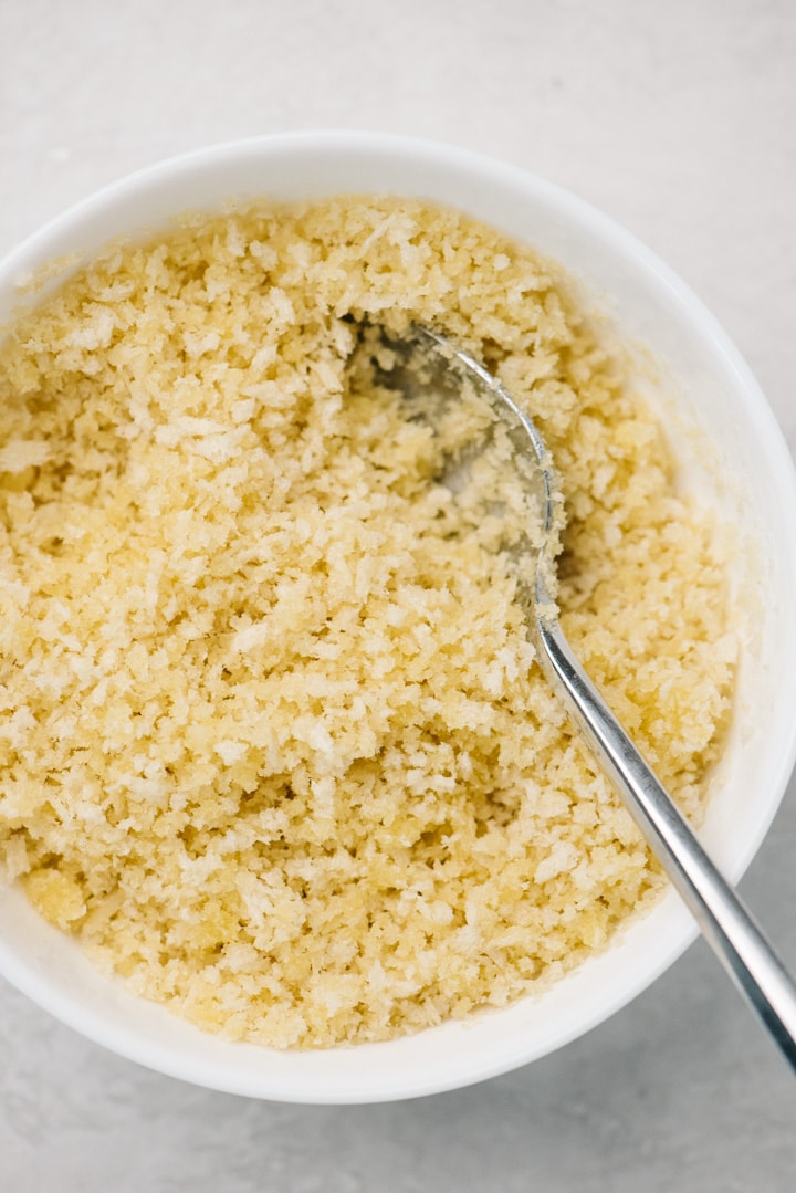 Breadcrumbs mixed with melted butter in a white bowl with a silver spoon.