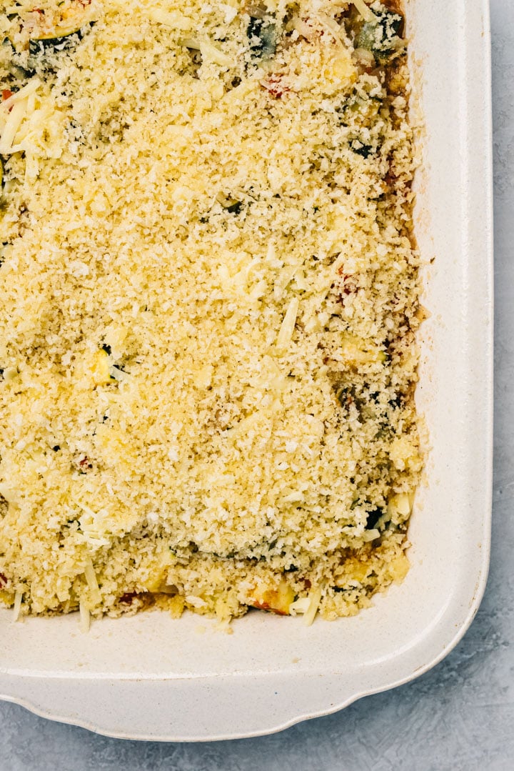 A zucchini casserole topped with cheese and breadcrumbs before baking.