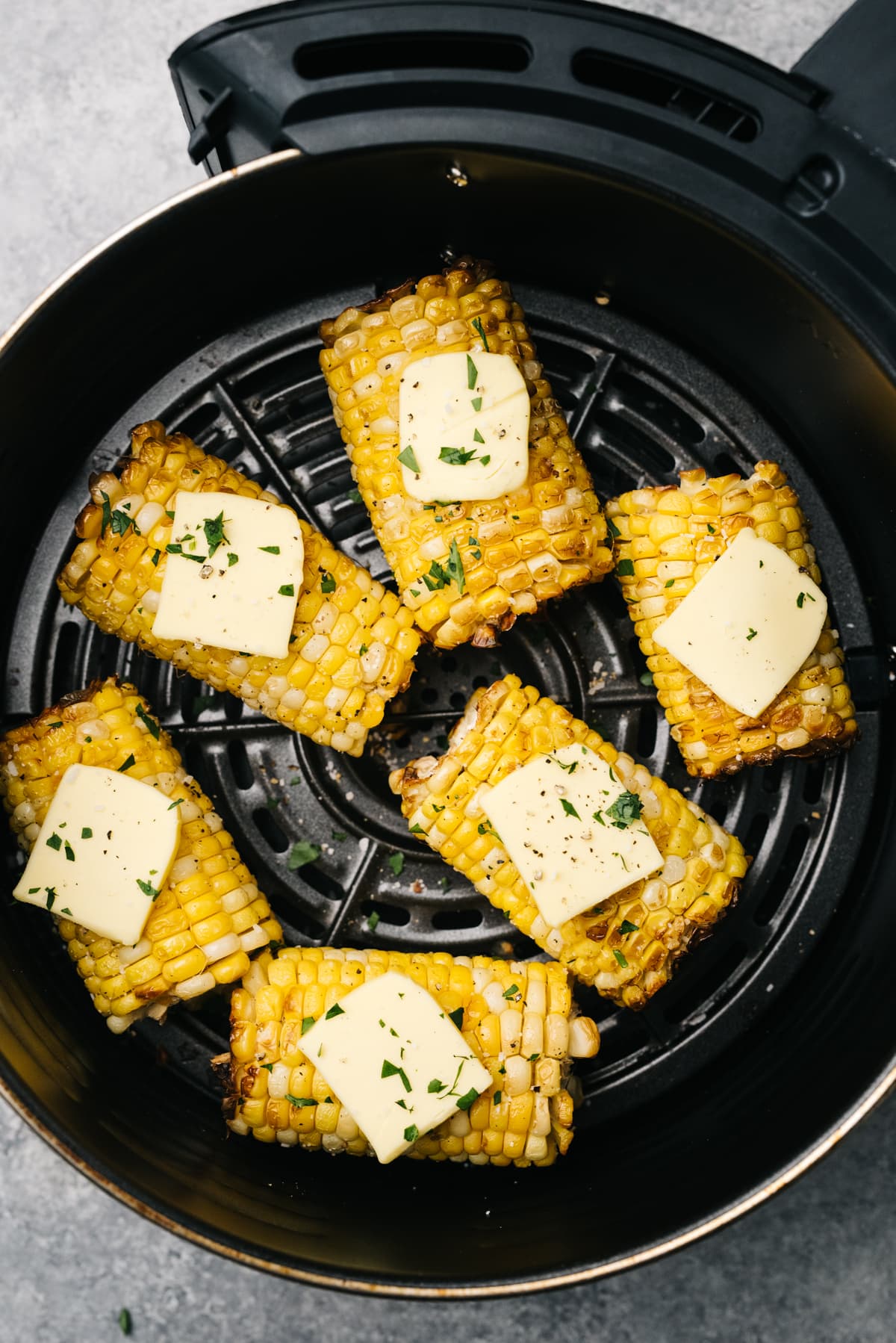 Air fryer corn on the cob in the basket of an air fryer, topped with butter and chopped basil.