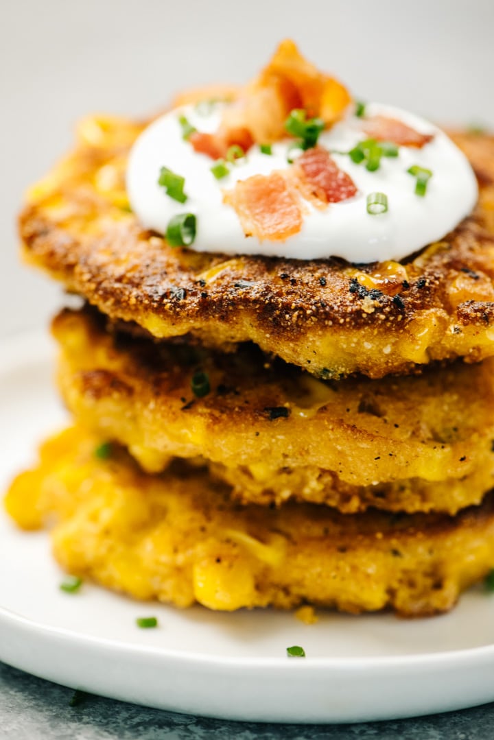 A stack of corn fritters topped with sour cream, bacon, and chives.