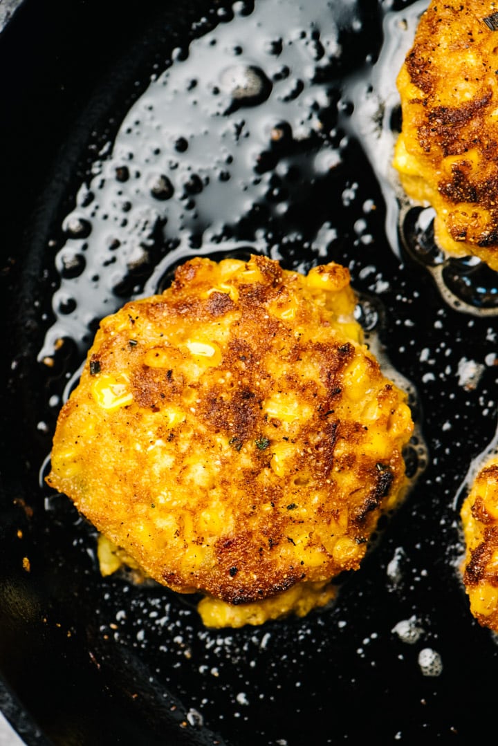 Golden brown corn fritters in a cast iron skillet.