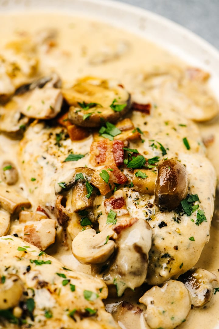 Side view, creamy mushroom chicken with bacon on a tan speckled plate, garnished with parsley.