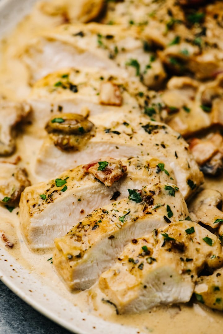 Creamy mushroom chicken sliced against the grain on a tan speckled plate.