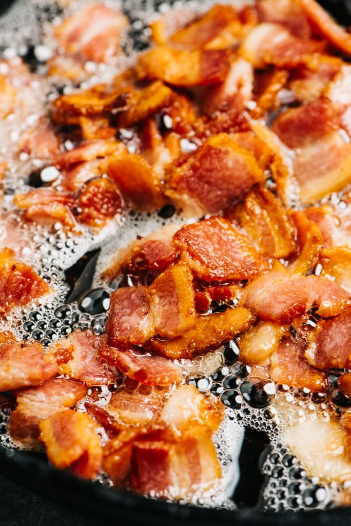 Chopped bacon frying in a skillet until golden brown.