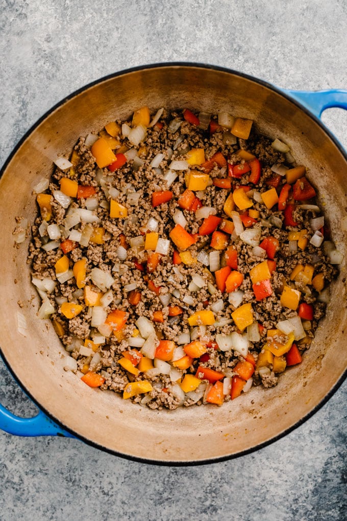 Ground beef sautéed with onions and bell peppers in a blue dutch oven.