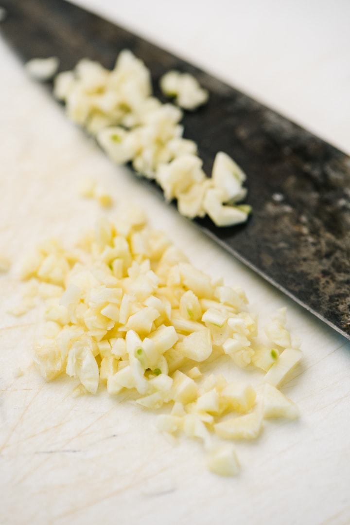 Roughly chopped garlic on a cutting board with a chef's knife.