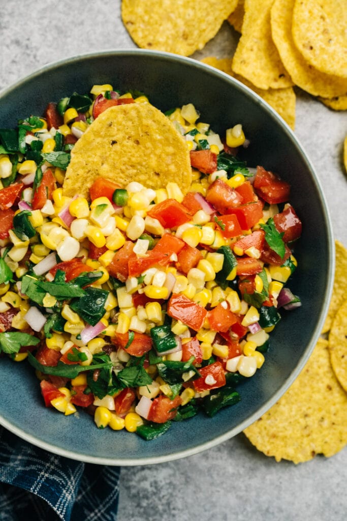 Roasted corn salsa in a blue bowl surrounded by tortilla chips.