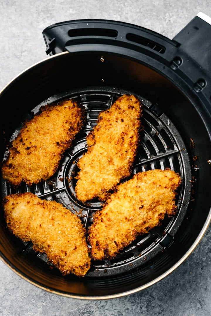 Four crispy chicken tenders in the basket of an air fryer.